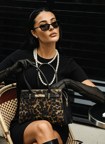Woman in black seated outdoors with the Leonora leopard calf hair bag resting on her lap