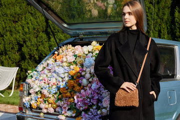 Woman wearing the Ivory Zita crossbody bag beside a car full of flowers