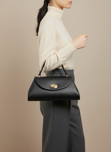 Woman carrying the Black Aveline flap bag by its top handle