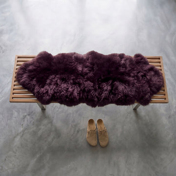 Aubergine double sheepskin throw in deep plum on a wooden bench, front view