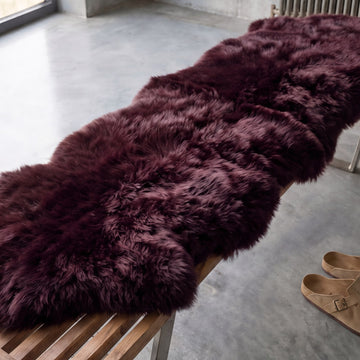 Close-up of deep plum Aubergine double sheepskin wool draped over a wooden bench
