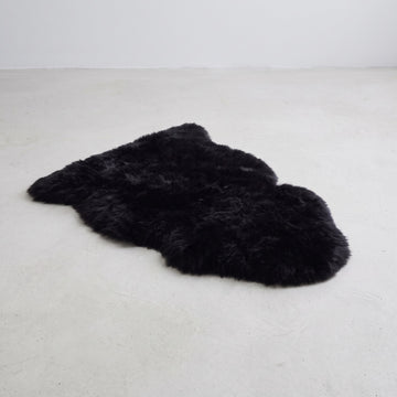 Black single sheepskin rug flat on a pale grey floor