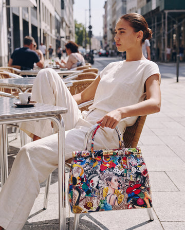 Woman with the Dalia leather top-handle bag by Clemés, pop-art print, seated at a sunlit café terrace