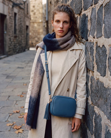 Model with the Navy Éloise Leather Tassel Camera Bag by Clemés on a stone-walled street with a scarf