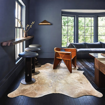 Tan and white cowhide rug styled on the floor of a moody dark blue living room