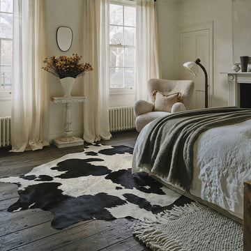 Speckled black and white cowhide rug styled on the floor of a warm neutral bedroom