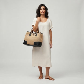 Model carrying the Black Ginevra Bamboo-Handle Raffia Bag by Clemés on her shoulder, studio shot