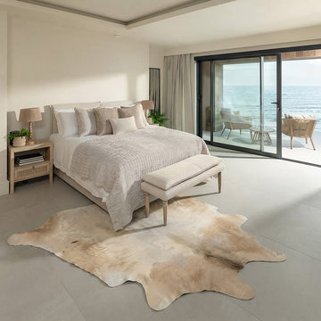 Tan and white cowhide rug styled on the floor of a coastal ocean-view bedroom