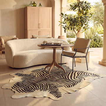 Zebra printed cowhide rug styled on the pale stone floor of a warm sunlit living room