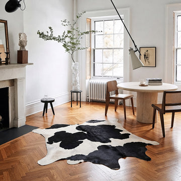 Espresso and ivory Holstein cowhide rug styled on the floor of a warm editorial dining nook