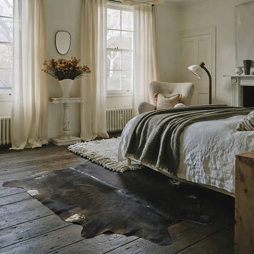 Espresso solid cowhide rug styled on the floor of a warm neutral bedroom