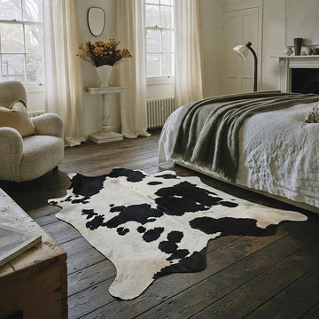 Black and white cowhide rug in a rustic wood-floor bedroom