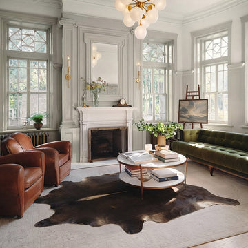 Dark chocolate cowhide rug in an elegant living room with green velvet sofa