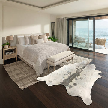 Ivory cowhide rug with grey dorsal stripe styled on the floor of a coastal ocean-view bedroom