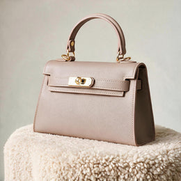 The Mini Kelly-Inspired Epsom Leather Handbag by Clemés in Dusty Rose, three-quarter studio shot on grey background