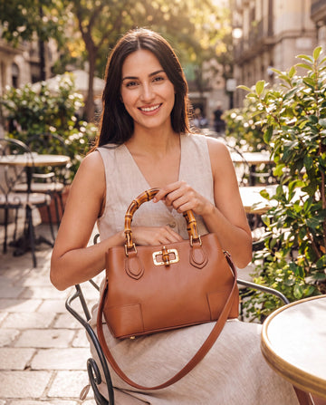 Woman with the Medium Ginevra bamboo-handle leather bag in Cognac at a sunlit café terrace