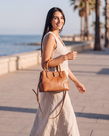 Woman with the Medium Ginevra bamboo-handle leather bag in Cognac on a seaside promenade