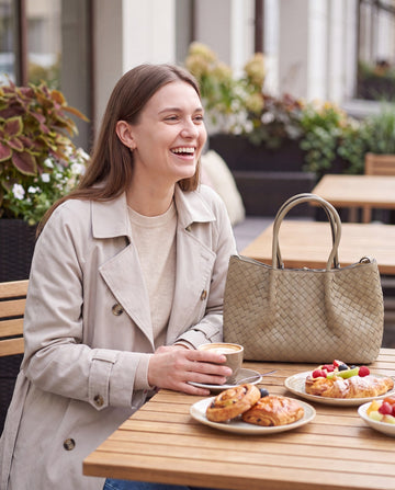 Woman with the Taupe Ornella woven leather bag at an outdoor brunch table