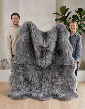 Two people holding up the Grey Sexto 6-pelt sheepskin rug to show its L180 x W150 cm size