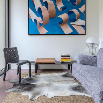 Grey cowhide rug styled over a jute rug in a contemporary living room with blue abstract art
