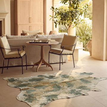 Acid-wash sage green cowhide rug styled on the stone floor of a warm neutral Mediterranean sitting room