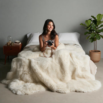 Ivory Octo New Zealand sheepskin rug throw styled on a bed, model holding a vintage camera