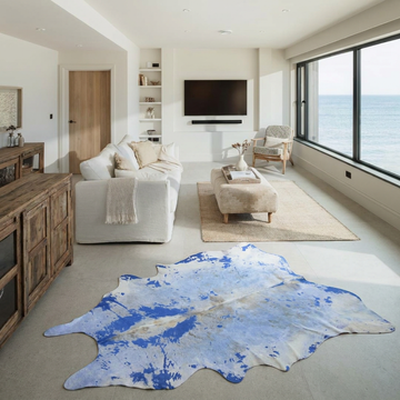 Blue acid wash cowhide rug styled on the stone floor of a coastal luxury living room with sea views
