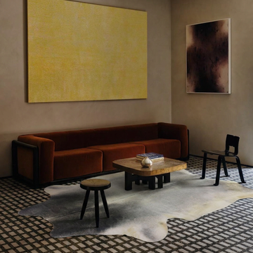 Grey cowhide rug styled on the mosaic floor of a warm minimalist living room with a rust sofa