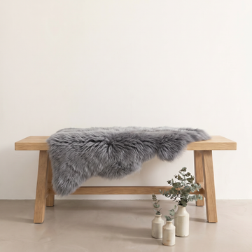 Grey sheepskin rug draped over an oak bench in a minimal interior