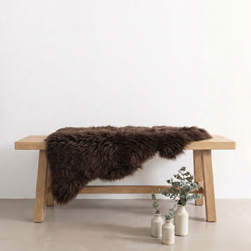 Chocolate sheepskin rug draped over an oak bench in a minimal interior