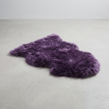 Purple single sheepskin rug laid flat on a pale grey floor