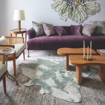 Platinum acid wash cowhide rug styled under curved wooden coffee tables in an elegant pale-grey living room