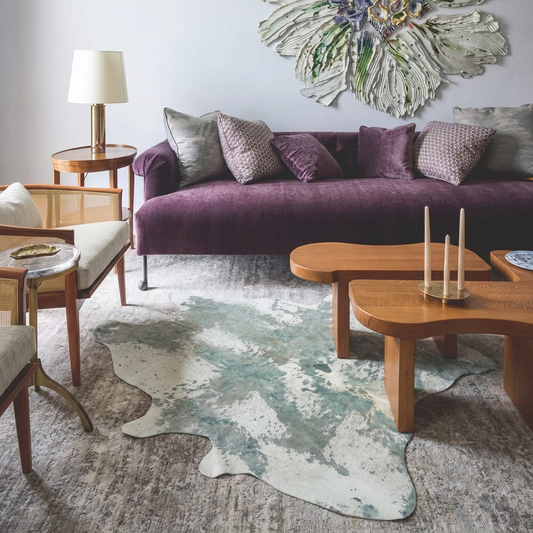 Platinum acid wash cowhide rug styled under curved wooden coffee tables in an elegant pale-grey living room
