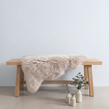 Oyster sheepskin rug draped over an oak bench in a minimal interior