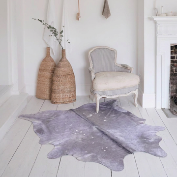 Lilac metallic cowhide rug styled on white painted floorboards in a soft romantic all-white sitting room