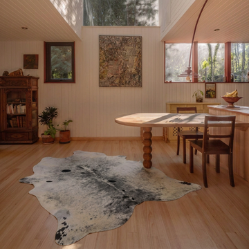 Salt and pepper grey cowhide rug styled on the pale wood floor of a bright Scandinavian dining room