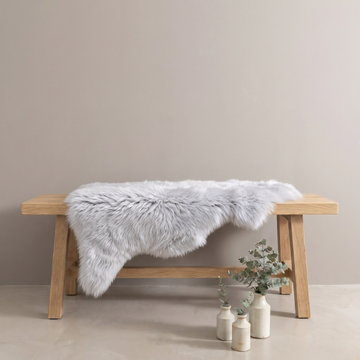 Silver sheepskin rug draped over an oak bench in a minimal interior