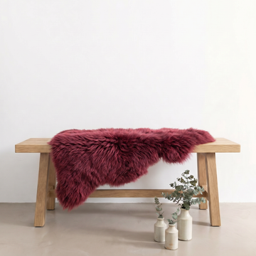 Raspberry sheepskin rug draped over an oak bench in a minimal interior