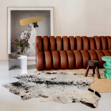 Black salt and pepper cowhide rug styled on the pale floor of a contemporary gallery-style lounge with tan leather sofa