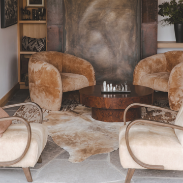 Tan and white cowhide rug styled between velvet armchairs by a game table