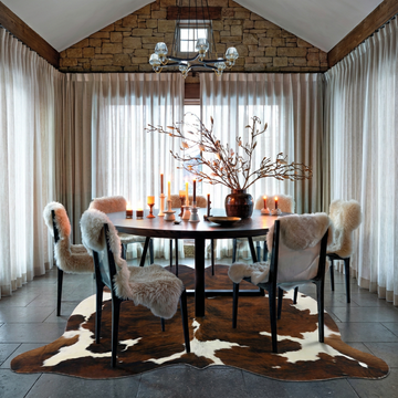 Tri colour brindle cowhide rug styled under the round table of a rustic stone-walled dining room