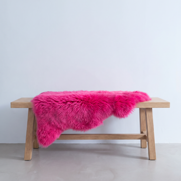 Fuchsia sheepskin rug draped over an oak bench in a minimal interior