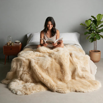 Champagne Octo New Zealand sheepskin rug throw styled on a bed, model reading a magazine