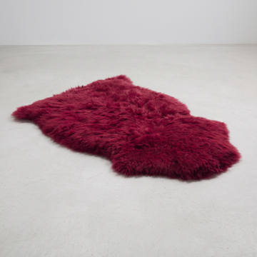 Raspberry single sheepskin rug laid flat on a pale grey floor