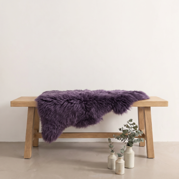 Purple sheepskin rug draped over an oak bench in a minimal interior