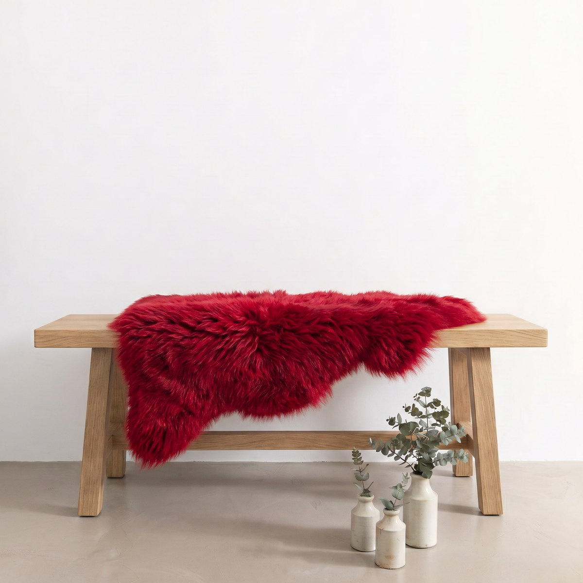 Wildfire red sheepskin rug draped over an oak bench in a minimal interior