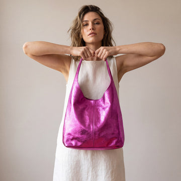 Model holding the Fuchsia Silvia Metallic Suede Slouch Bag up by its handle with both hands, studio shot