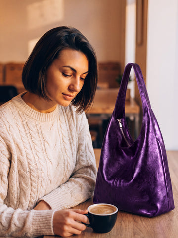 Violet Silvia Metallic Suede Slouch Bag on a table in a cosy café