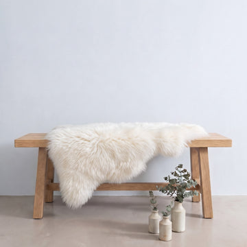 Ivory sheepskin rug draped over an oak bench in a minimal interior