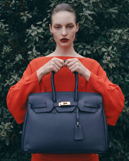Model in a red knit holding the Navy Valentina Maxi Leather Tote against dark foliage